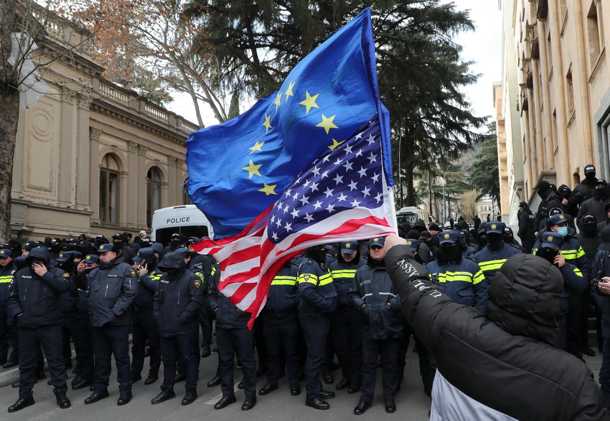 Участник акции протеста у здания парламента Грузии держит флаги ЕС и США, Тбилиси, 29 декабря 2024 года. Фото: David Mdzinarishvili / EPA