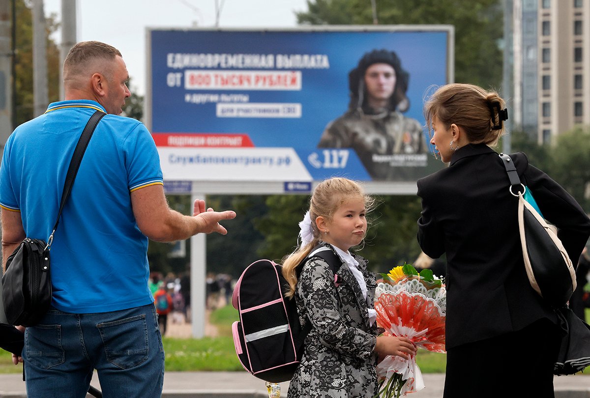 Школьница и ее родители проходят мимо плаката с изображением российского солдата и рекламой призыва на военную службу. Фото: Анатолий Мальцев / EPA-EFE