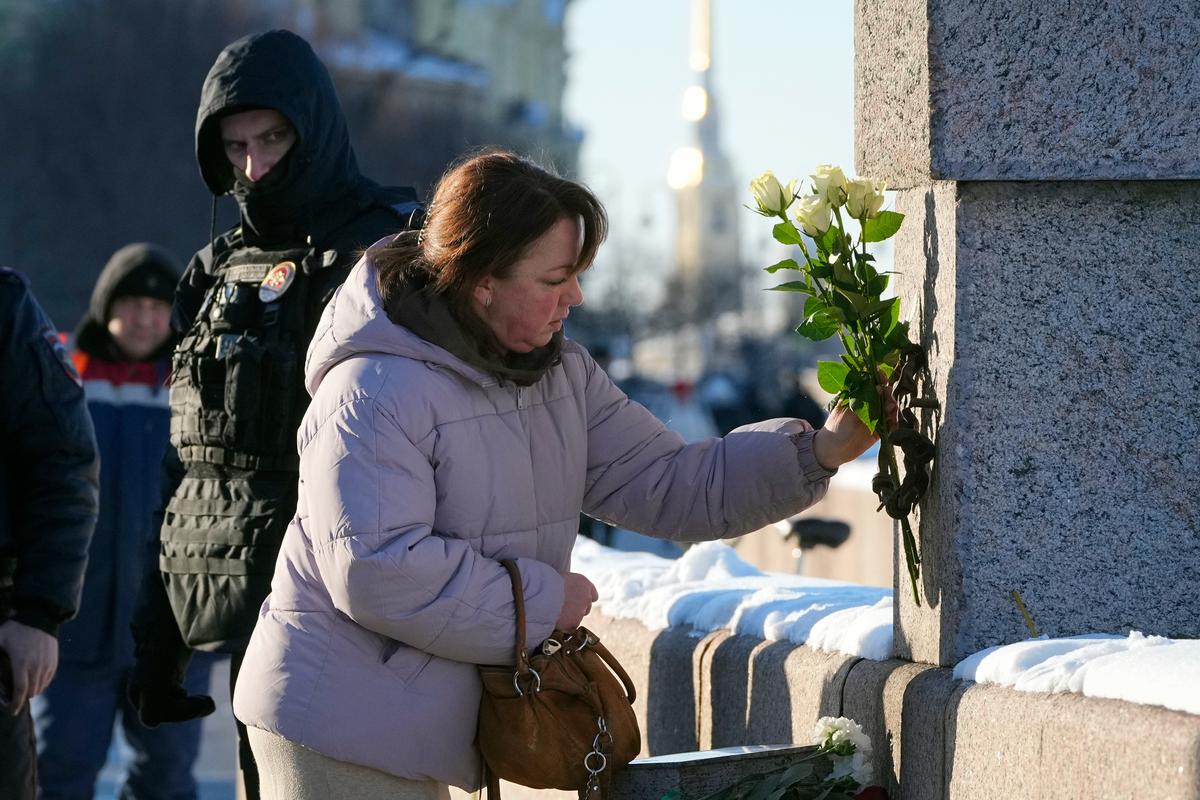 Полицейский наблюдает за женщиной, возлагающим цветы в память об Алексее Навальном у Мемориала жертвам политических репрессий, Санкт-Петербург, 16 февраля 2025 года. Фото: AP Photo / Scanpix / LETA